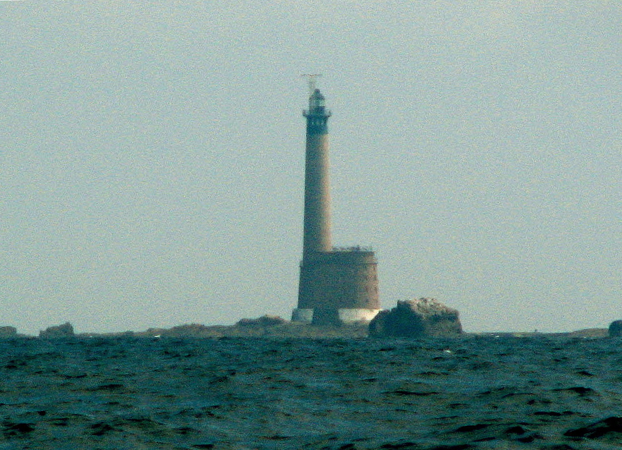 Roches-Douvres Lighthouse rising from its low rocky plateau across open water.